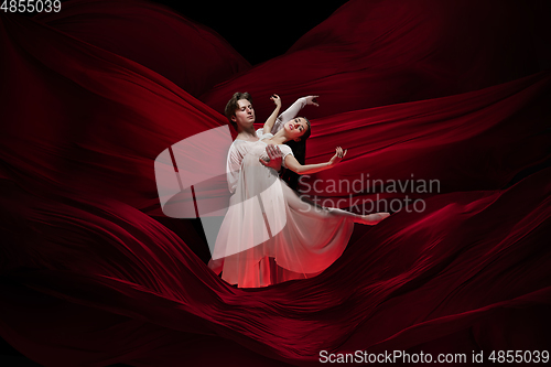 Image of Young and graceful ballet dancers on billowing red cloth background in classic action. Art, motion, action, flexibility, inspiration concept.