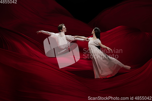 Image of Young and graceful ballet dancers on billowing red cloth background in classic action. Art, motion, action, flexibility, inspiration concept.