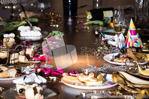 Image of Early morning after the party. Glasses and plates on the table with confetti and serpentine, leftovers, flower petals