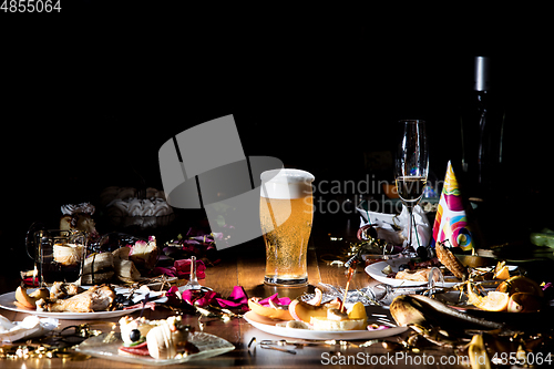 Image of Early morning after the party. Glass of light, cold lager, beer on the table with confetti and serpentine, leftovers, flower petals