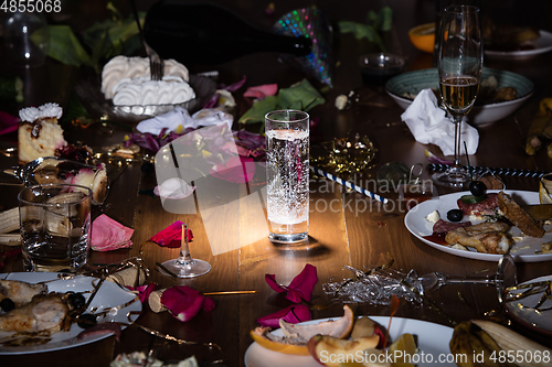 Image of Early morning after the party. Glass of pure, cold water on the table with confetti and serpentine, leftovers, flower petals