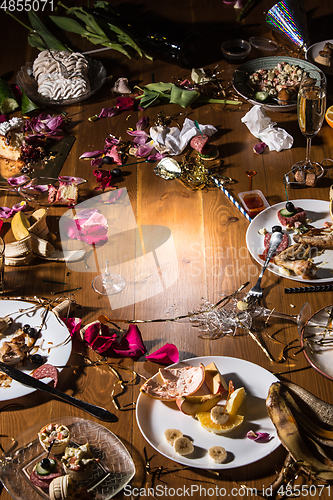 Image of Early morning after the party. Glasses and plates on the table with confetti and serpentine, leftovers, flower petals