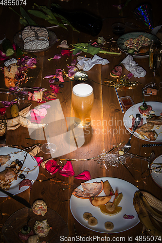 Image of Early morning after the party. Glass of light, cold lager, beer on the table with confetti and serpentine, leftovers, flower petals