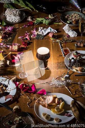 Image of Early morning after the party. Glass of dark, cold stout, beer on the table with confetti and serpentine, leftovers, flower petals