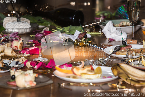 Image of Early morning after the party. Glasses and plates on the table with confetti and serpentine, leftovers, flower petals