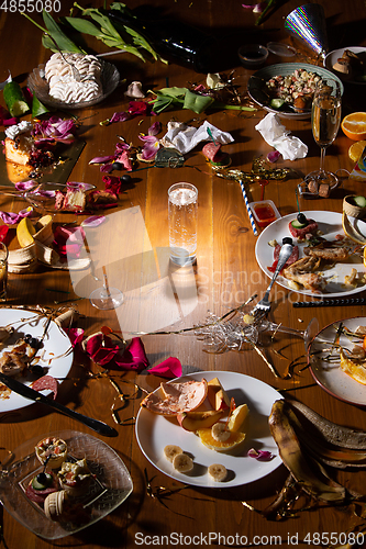 Image of Early morning after the party. Glass of pure, cold water on the table with confetti and serpentine, leftovers, flower petals