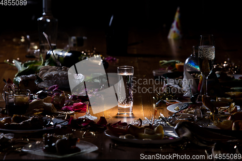 Image of Early morning after the party. Glass of pure, cold water on the table with confetti and serpentine, leftovers, flower petals