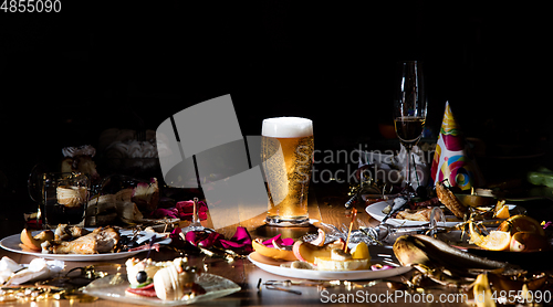 Image of Early morning after the party. Glass of light, cold lager, beer on the table with confetti and serpentine, leftovers, flower petals