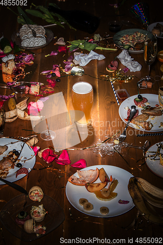 Image of Early morning after the party. Glass of light, cold lager, beer on the table with confetti and serpentine, leftovers, flower petals