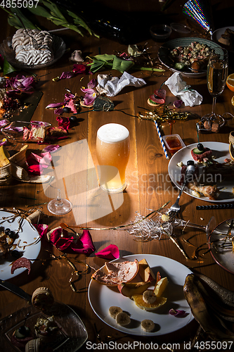 Image of Early morning after the party. Glass of light, cold lager, beer on the table with confetti and serpentine, leftovers, flower petals