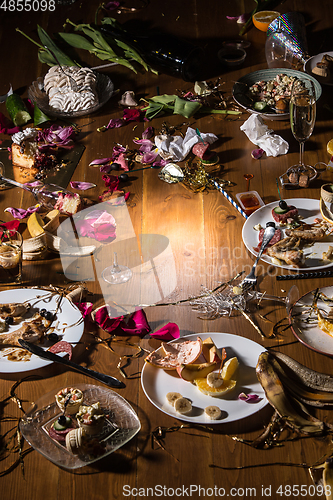 Image of Early morning after the party. Glasses and plates on the table with confetti and serpentine, leftovers, flower petals