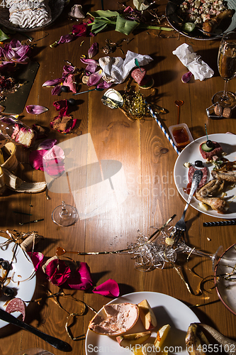 Image of Early morning after the party. Glasses and plates on the table with confetti and serpentine, leftovers, flower petals