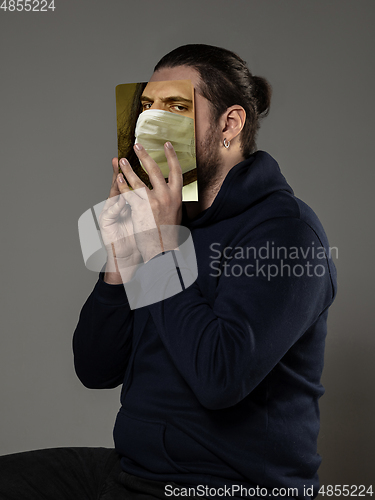 Image of Be safe and read to become someone else - man covering face with book in face mask while reading on grey background