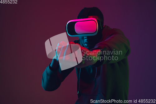 Image of African-american man\'s portrait in VR-headset isolated on gradient studio background in neon light