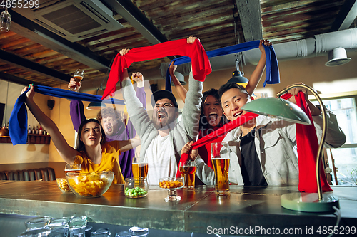 Image of Sport fans cheering at bar, pub and drinking beer while championship, competition is going