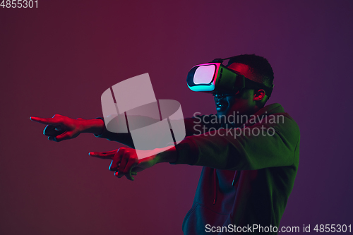 Image of African-american man\'s portrait in VR-headset isolated on gradient studio background in neon light