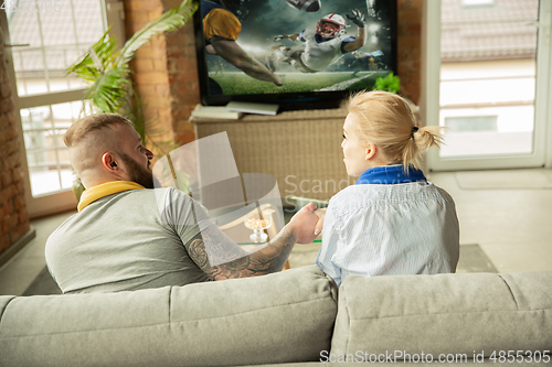 Image of Excited family watching american football, sport match at home, beautiful couple