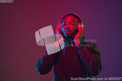 Image of African-american man\'s portrait with headphones isolated on gradient studio background in neon light