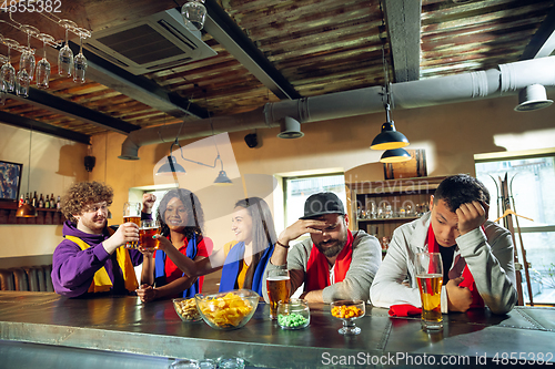 Image of Sport fans cheering at bar, pub and drinking beer while championship, competition is going