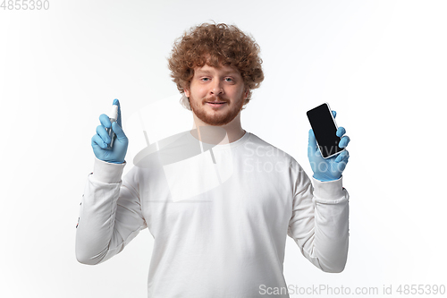 Image of How coronavirus changed our lives. Young man disinfecting gadgets surfaces on white background