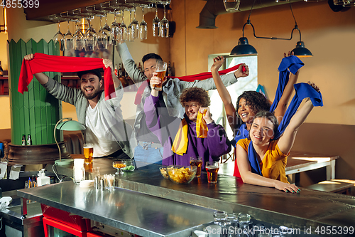 Image of Sport fans cheering at bar, pub and drinking beer while championship, competition is going