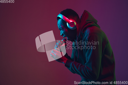 Image of African-american man\'s portrait with headphones isolated on gradient studio background in neon light