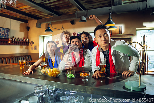 Image of Sport fans cheering at bar, pub and drinking beer while championship, competition is going