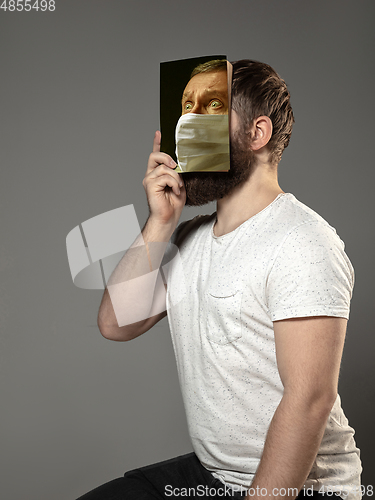 Image of Be safe and read to become someone else - man covering face with book in face mask while reading on grey background