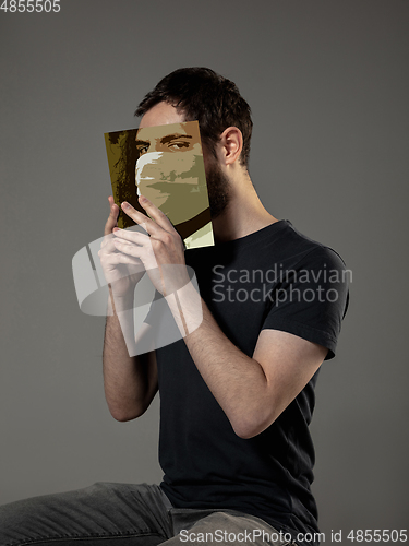 Image of Be safe and read to become someone else - man covering face with book in face mask while reading on grey background