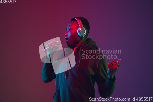 Image of African-american man\'s portrait with headphones isolated on gradient studio background in neon light