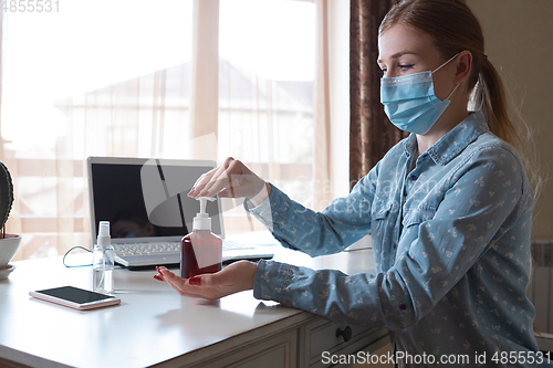 Image of Young woman in face mask disinfecting gadgets surfaces on her workplace