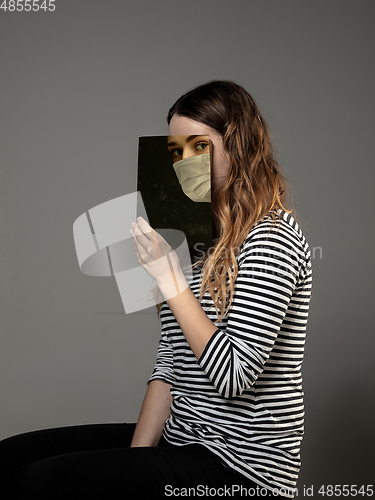 Image of Be safe and read to become someone else - woman covering face with book in face mask while reading on grey background