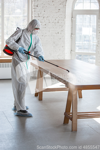 Image of Coronavirus Pandemic. A disinfector in a protective suit and mask sprays disinfectants in the house or office