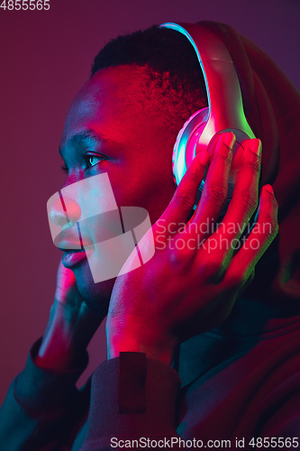 Image of African-american man\'s portrait with headphones isolated on gradient studio background in neon light
