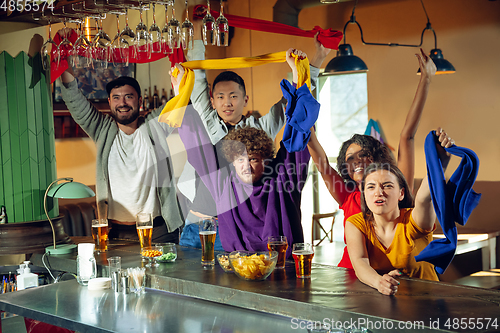 Image of Sport fans cheering at bar, pub and drinking beer while championship, competition is going