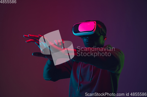 Image of African-american man\'s portrait in VR-headset isolated on gradient studio background in neon light