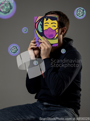 Image of Be safe and read to become someone else - man covering face with book in face mask while reading on grey background