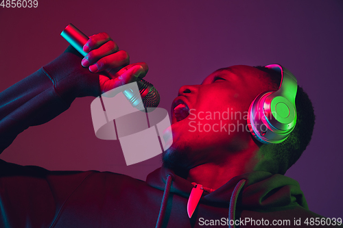Image of African-american man\'s portrait with headphones isolated on gradient studio background in neon light