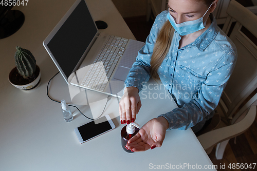 Image of Young woman in face mask disinfecting gadgets surfaces on her workplace