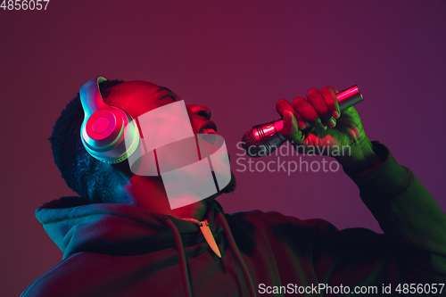 Image of African-american man\'s portrait with headphones isolated on gradient studio background in neon light
