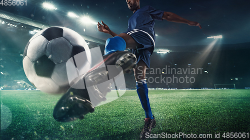 Image of Football or soccer player in action on stadium with flashlights, kicking ball for winning goal, wide angle