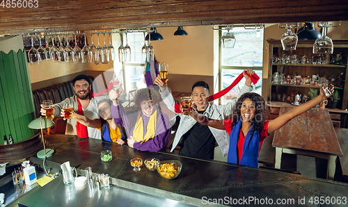 Image of Sport fans cheering at bar, pub and drinking beer while championship, competition is going