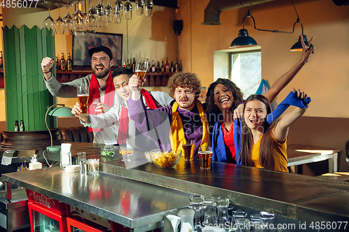 Image of Sport fans cheering at bar, pub and drinking beer while championship, competition is going