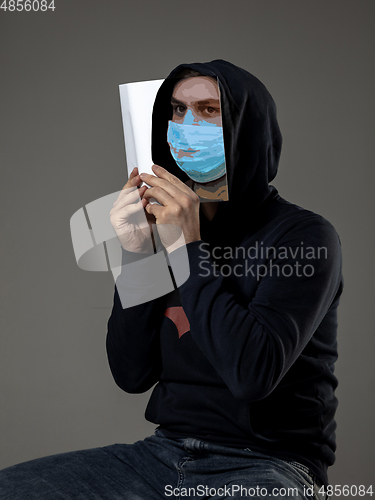 Image of Be safe and read to become someone else - man covering face with book in face mask while reading on grey background