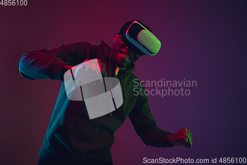 Image of African-american man\'s portrait in VR-headset isolated on gradient studio background in neon light