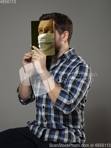 Image of Be safe and read to become someone else - man covering face with book in face mask while reading on grey background