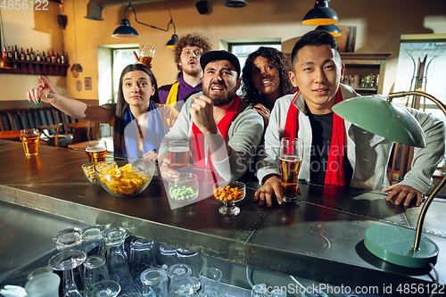 Image of Sport fans cheering at bar, pub and drinking beer while championship, competition is going