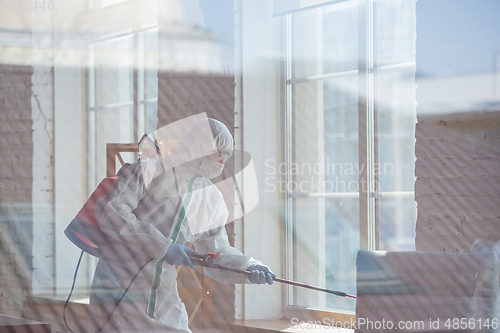 Image of Coronavirus Pandemic. A disinfector in a protective suit and mask sprays disinfectants in the house or office