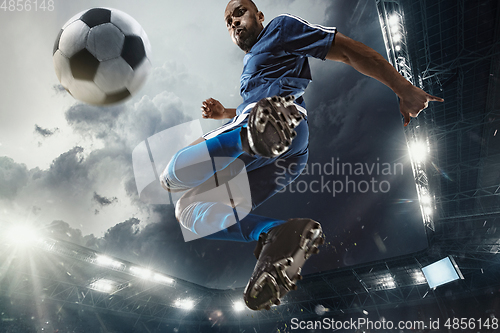 Image of Football or soccer player in action on stadium with flashlights, kicking ball for winning goal, wide angle