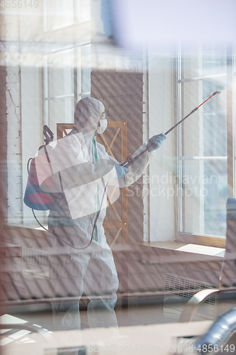 Image of Coronavirus Pandemic. A disinfector in a protective suit and mask sprays disinfectants in the house or office